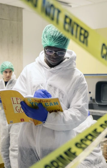 Forensic science student reads instructions behind crime scene tape during a practical lab exercise. Forensic science student reads instructions behind crime scene tape during a practical lab exercise.